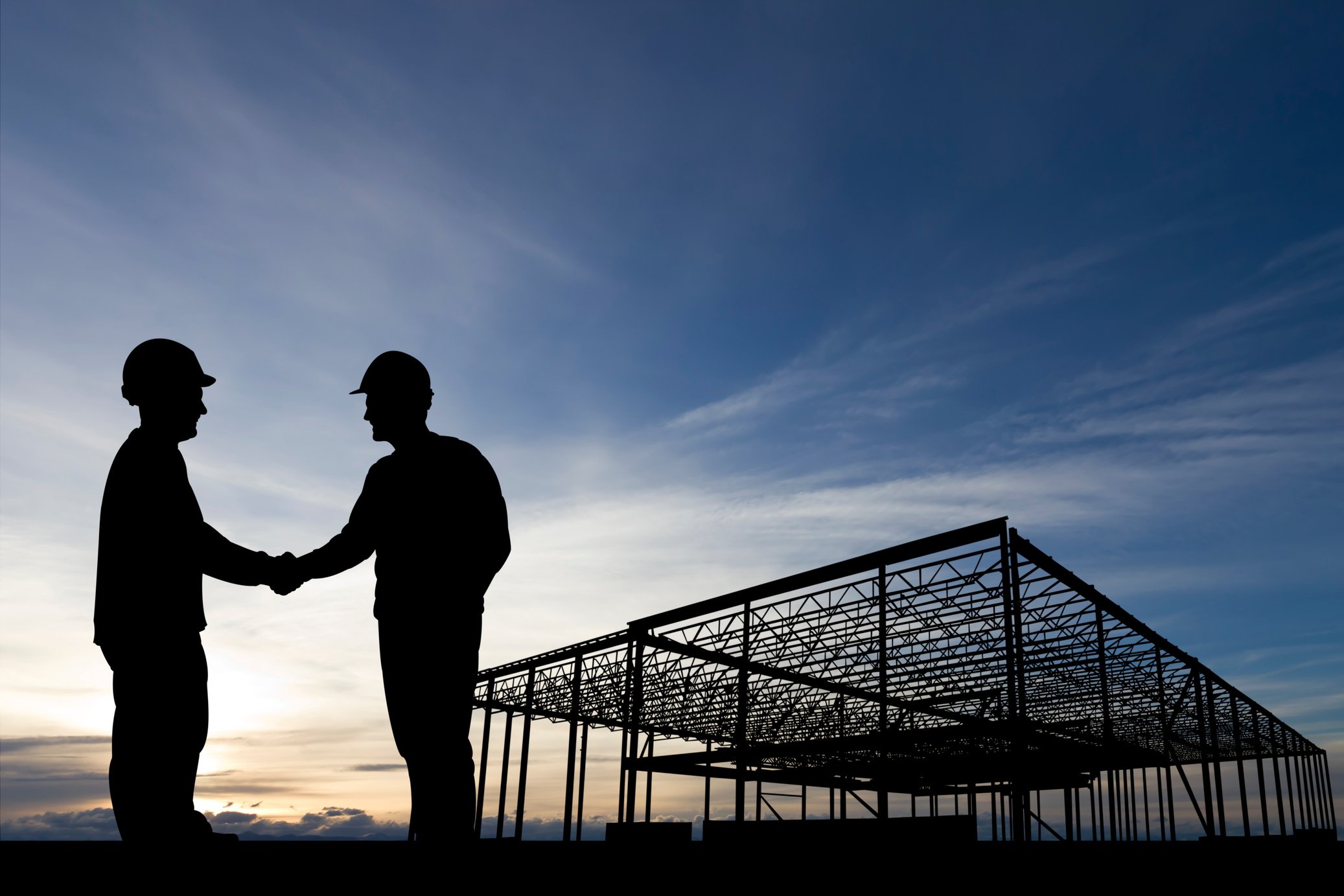 Two individuals shaking hands in front of a building under construction.