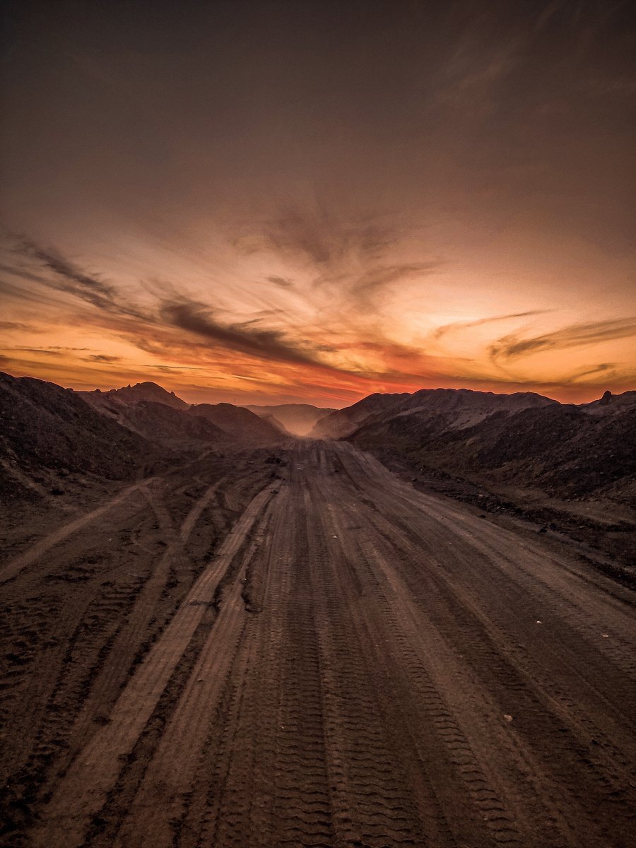 an aerial view of a dirt road in the desert at sunset